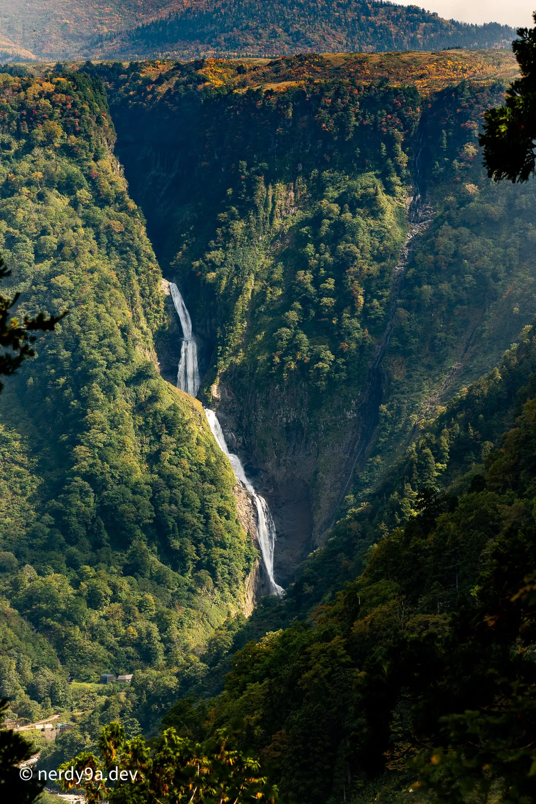 Distant view of Shomyo Falls cascading down a deep V-shaped green mountain gorge