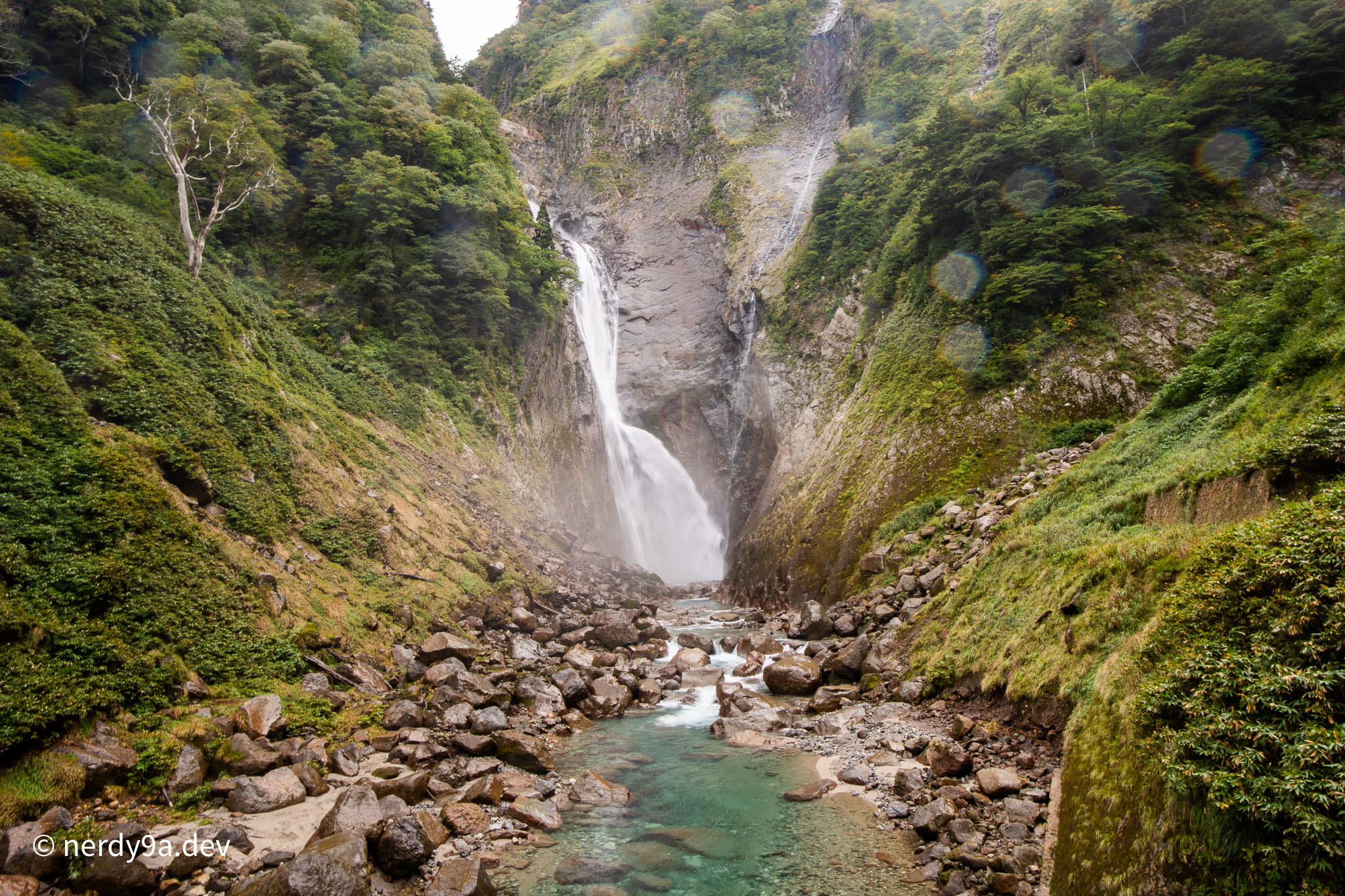 Close-up of Shomyo Falls plunging down a rocky cliff face into a clear turquoise river basin