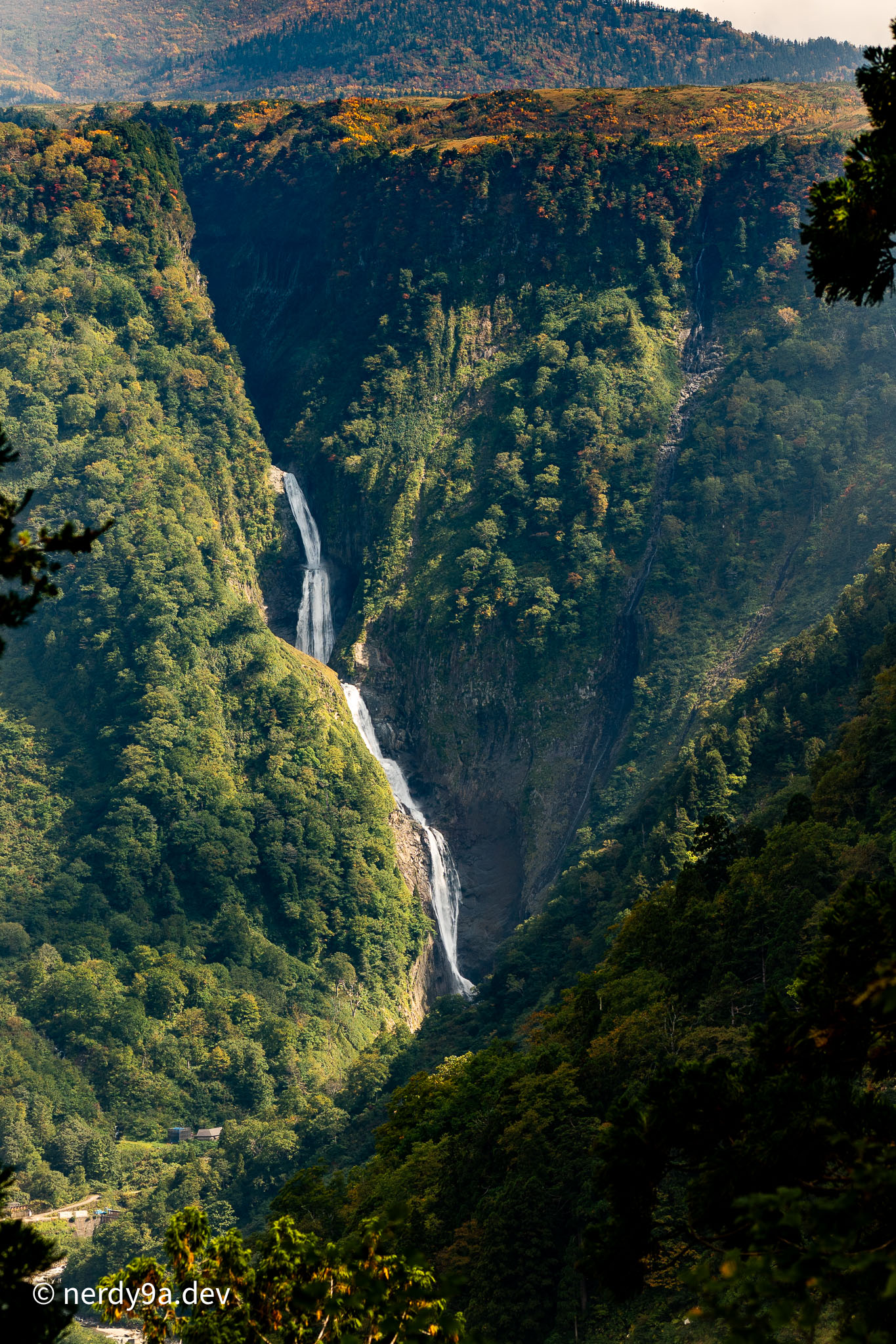 Distant view of Shomyo Falls cascading down a deep V-shaped green mountain gorge