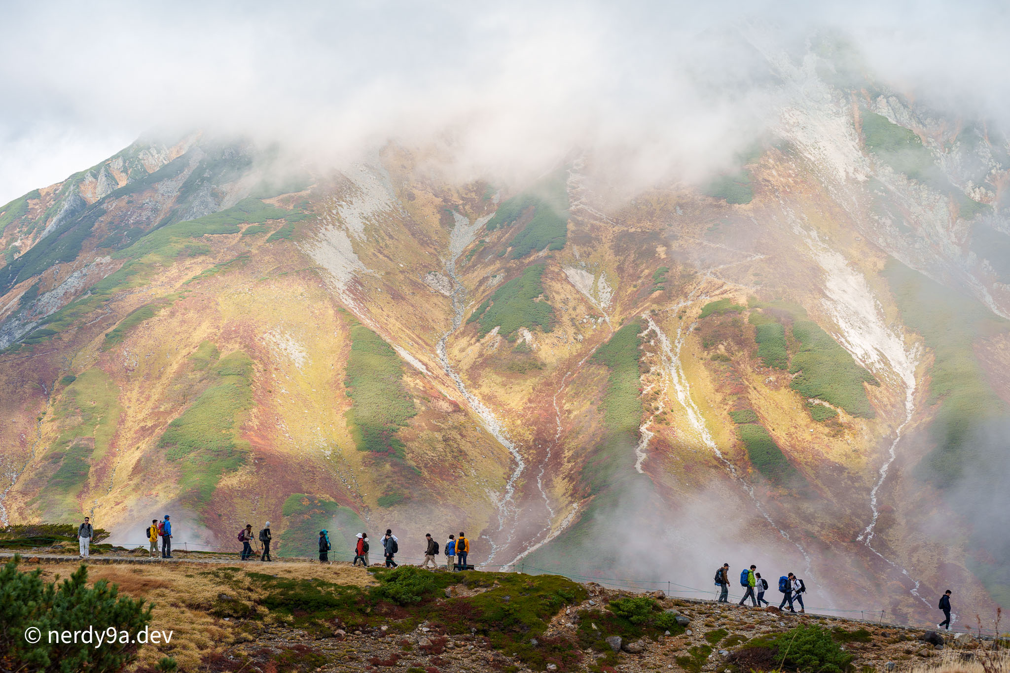 Tourists hiking on the alpine trail at Murodo with volcanic steam vents rising and autumn colors on mountain slopes