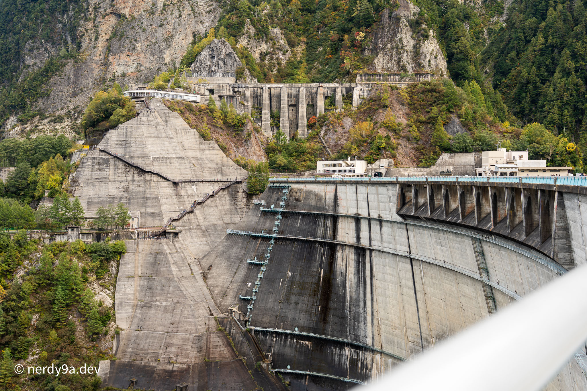 The massive concrete structure of Kurobe Dam with stairs leading up the steep mountain side to the observation deck