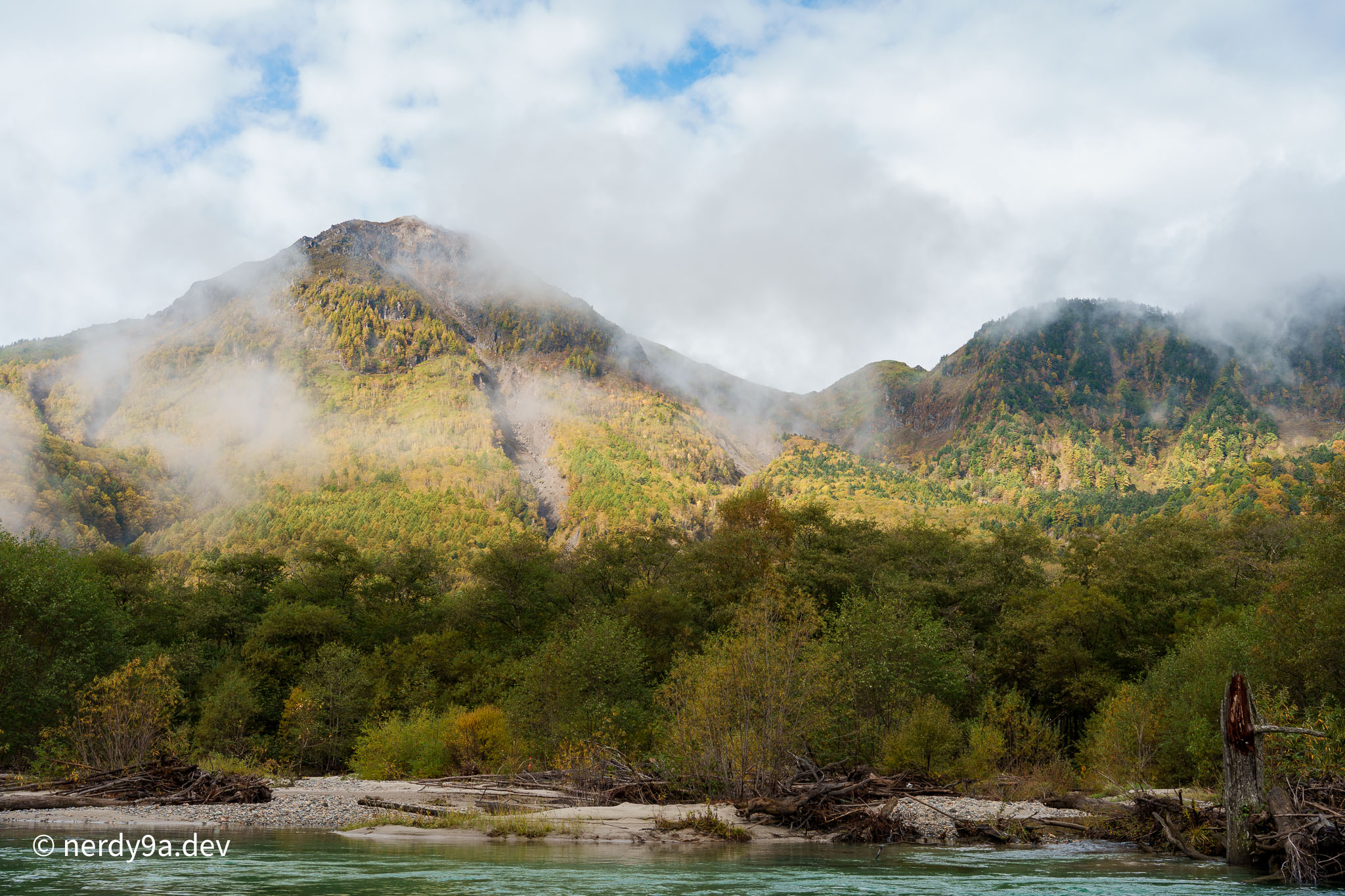 Standing dead trees reflected in the calm waters of Taisho Pond under autumn-colored mountains